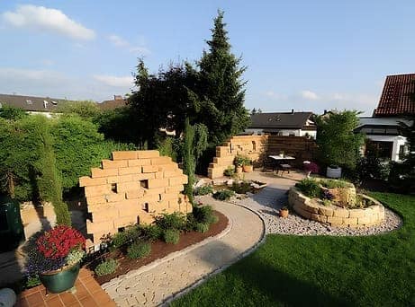 Jardin paysager avec murets en pierre, allée pavée, massifs et pelouse.